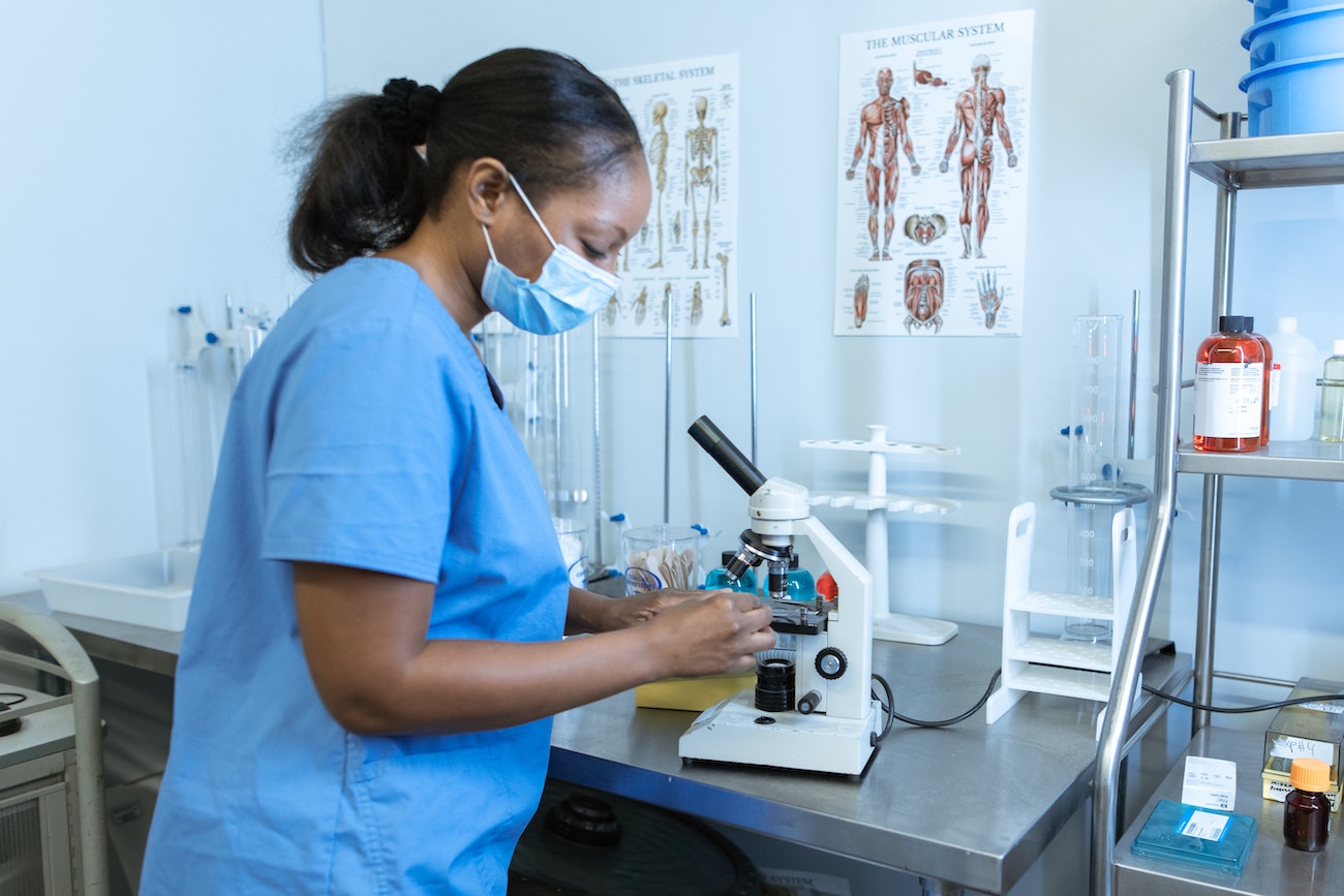 A person wearing a mask in a science lab looking at samples under a microscope