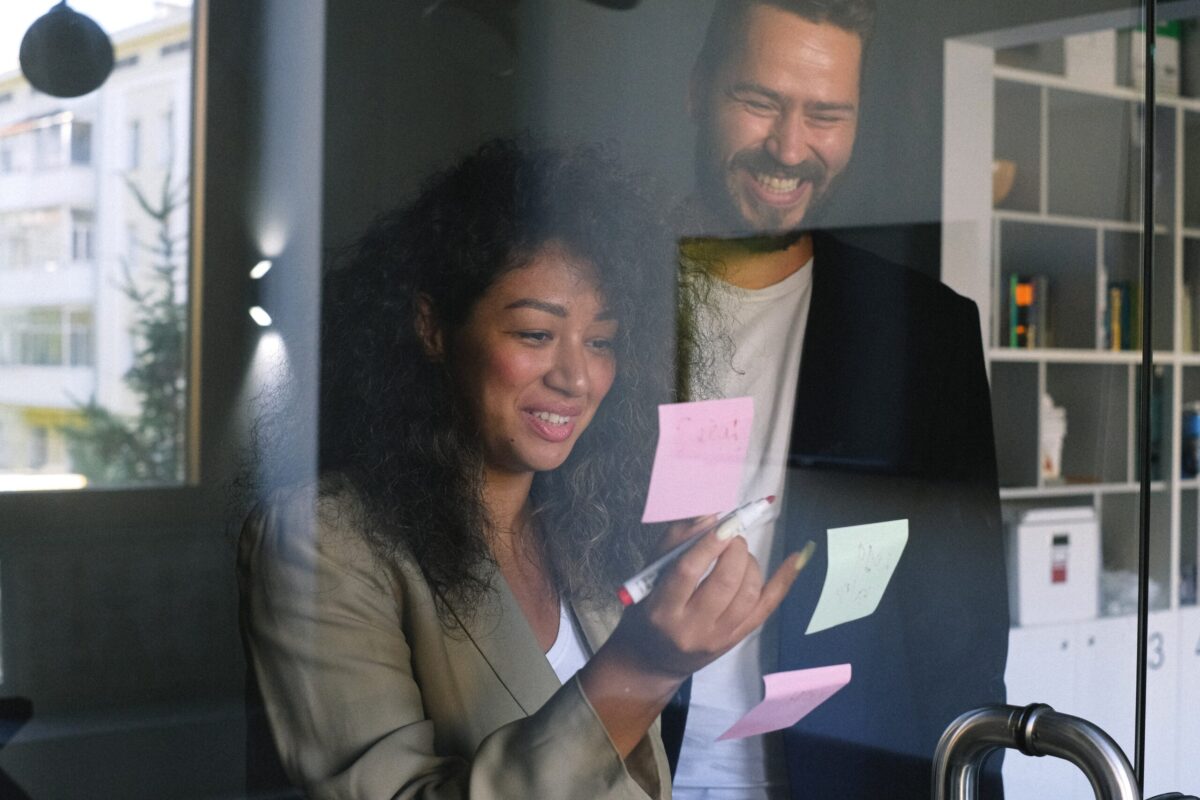 a man and a woman looking at post it notes on a clear wall